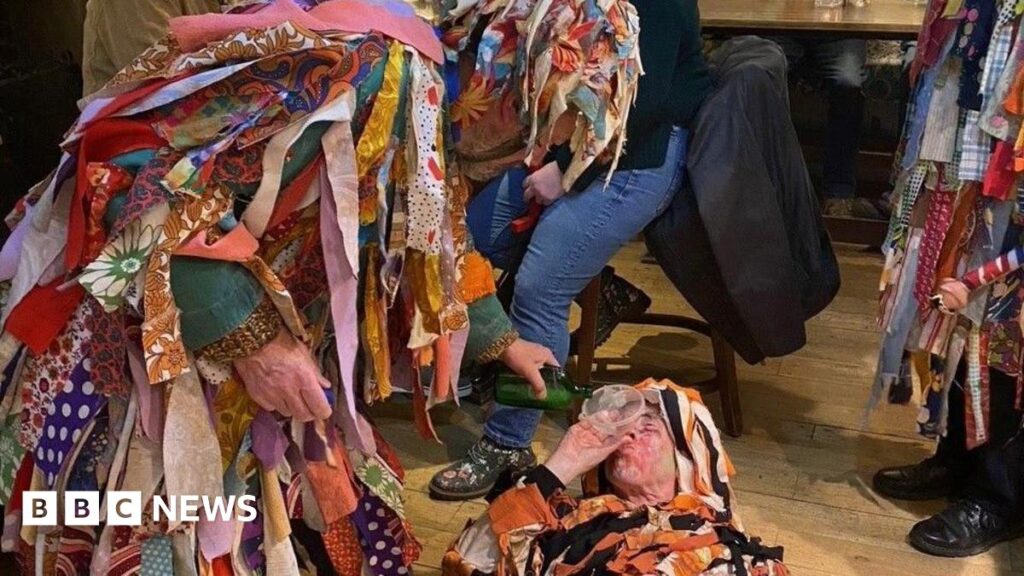 Chewit Well Mummers raise hundreds touring Yorkshire pubs Three figures in coats covered in rags perform a play on a pub floor. One is laying on the ground with a funnel in his mouth while another pours liquid from a green bottle.