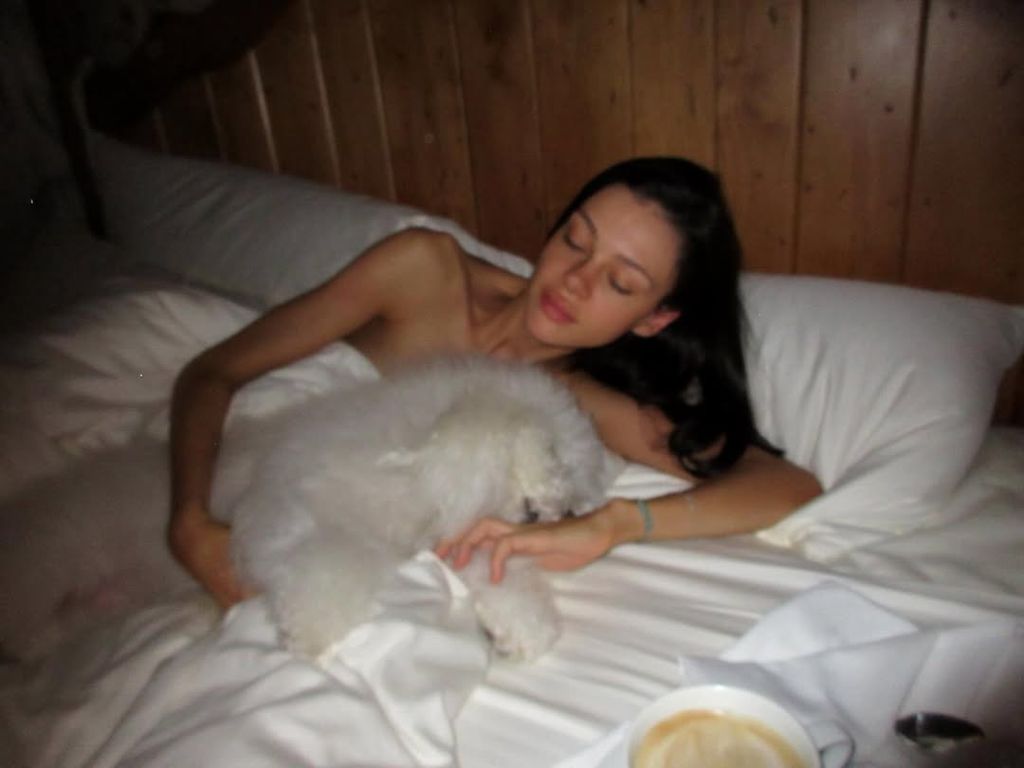woman in white bed with fluffy white dog
