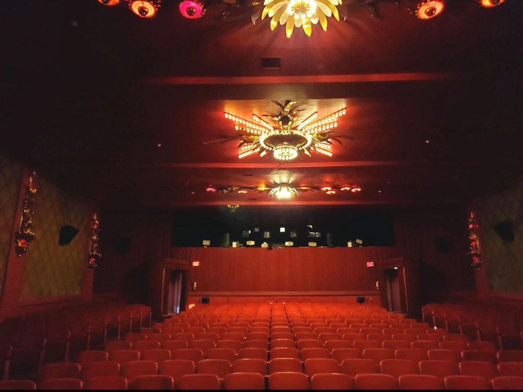 Interior of the Fine Arts Beverly Hills Theatre with rows of empty red seats and ornate ceiling lights.
