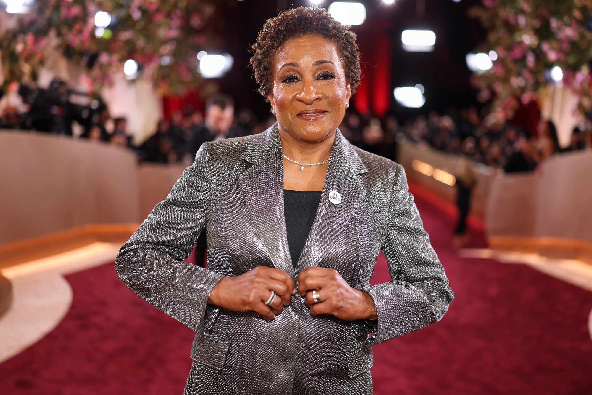 Wanda Sykes poses on the red carpet, wearing a Be Good on her suit jacket.