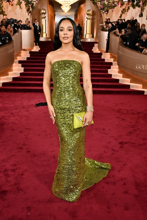 Tessa Thompson holds a green clutch bag with two #BeGood pins, reading 