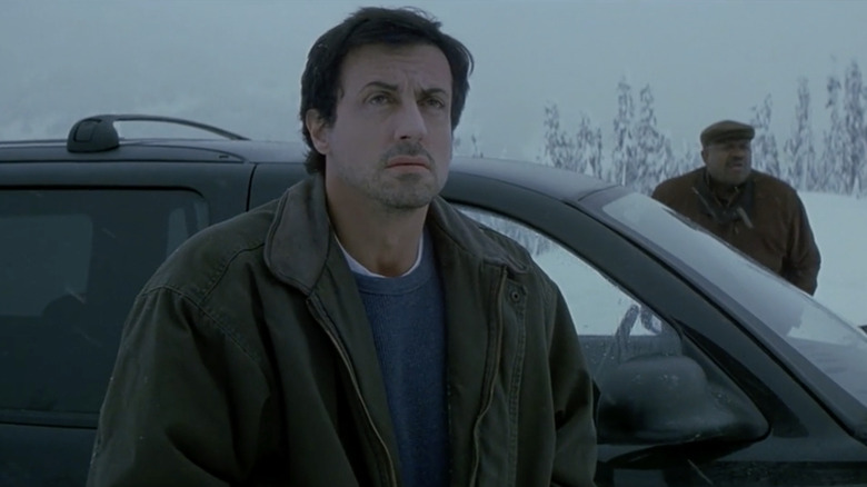 Sylvester Stallone as Jake Malloy stands outside an SUV in the snow, with Charles S. Dutton as Chuck Hendricks behind him, in D-Tox