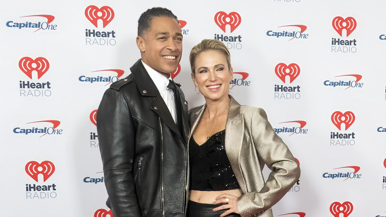 T.J. Holmes wearing a leather jacket and Amy Robach wearing a black crop top and gold jacket
