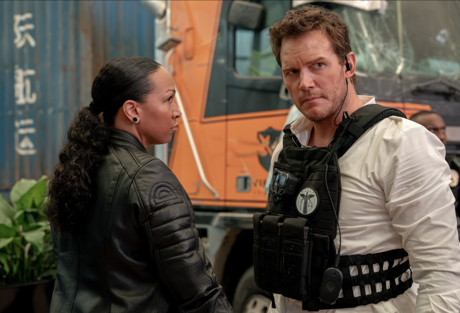 Movie Review: ‘Mercy,’ Starring Chris Pratt A Black woman wearing a black leather jacket with her hair tied back in a long ponytail, eyes a white man suspiciously. He is wearing a white shirt with a black tactical vest on top.
