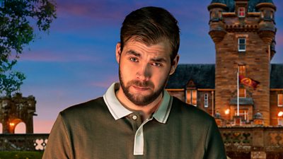 A young man in a polo shirt looks to camera with an eyebrow raised, set against the backdrop of a castle by night