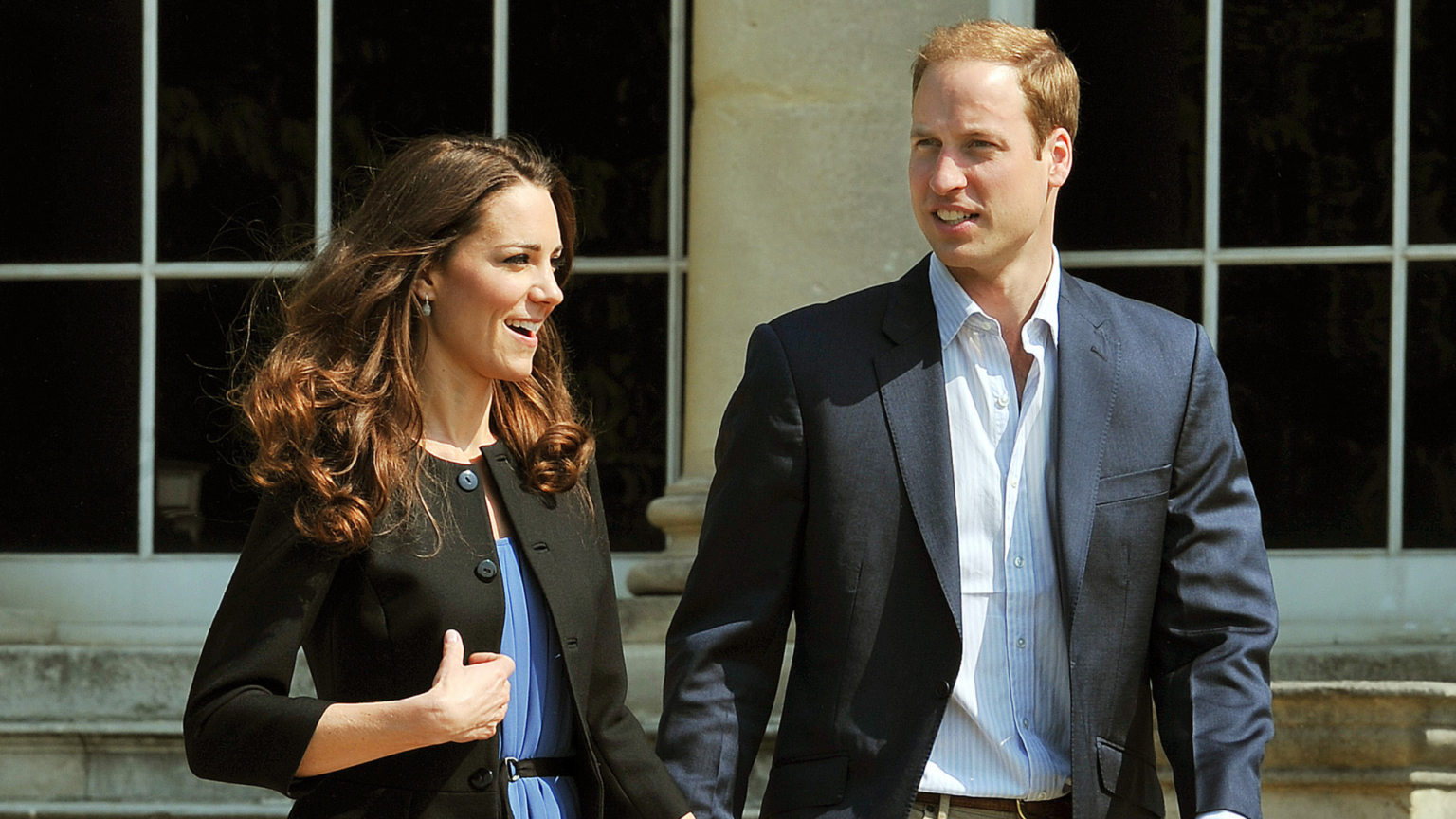 Prince William and Princess Kate Took a Secret Honeymoon Trip That “Was Never Discovered or Written About” Princess Kate wearing a black blazer and blue dress holding walking next to Prince William
