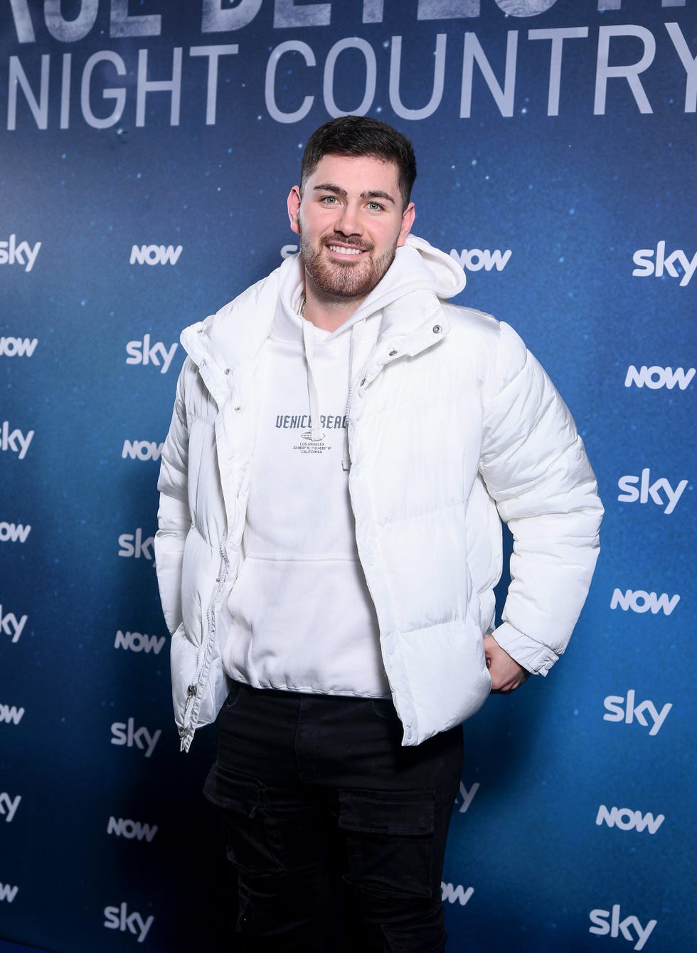 individual poses in front of a promotional backdrop