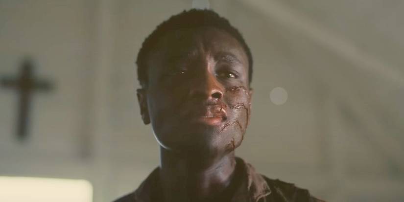 A closeup shot of Miles Caton as Churchboy with a bloody gash on his face, while standing in a white chapel, in Sinners.