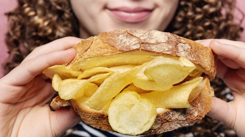 A woman preparing to eat a crisp/chip sandwich.