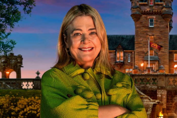 An image of a woman smiling ahead with her arms folded in front of her chest. She is wearing a green jacket.