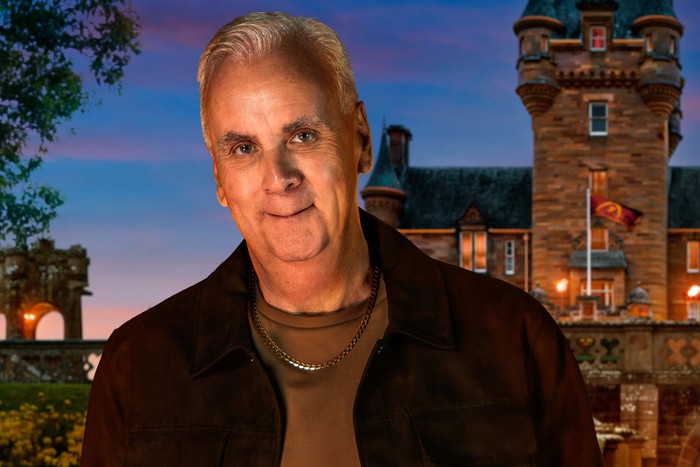 A man smiling ahead, wearing a brown t-shirt and jacket.