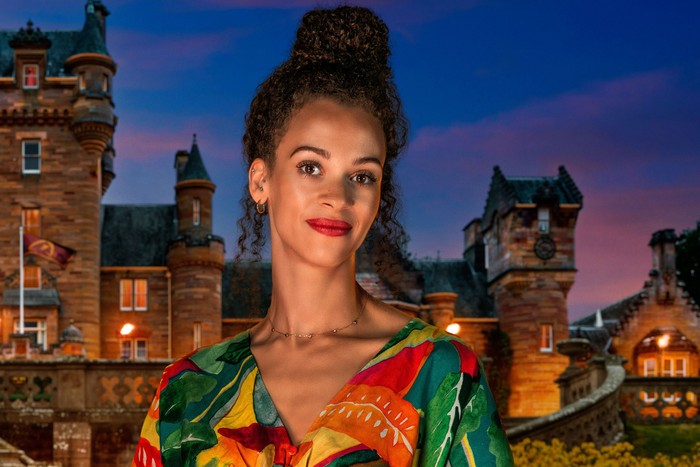 A woman smiling ahead, wearing a multicoloured blouse.