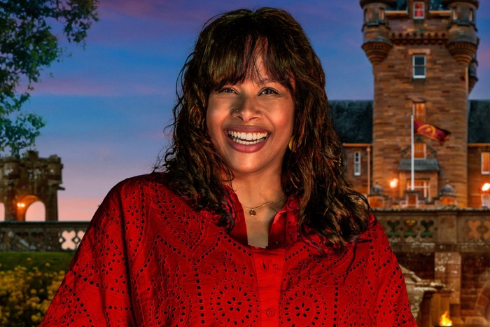 An image of a woman smiling ahead, wearing a red blouse.