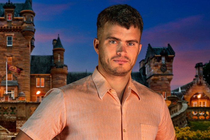 A man looking ahead with a serious expression on his face. He is wearing a light pink shirt.