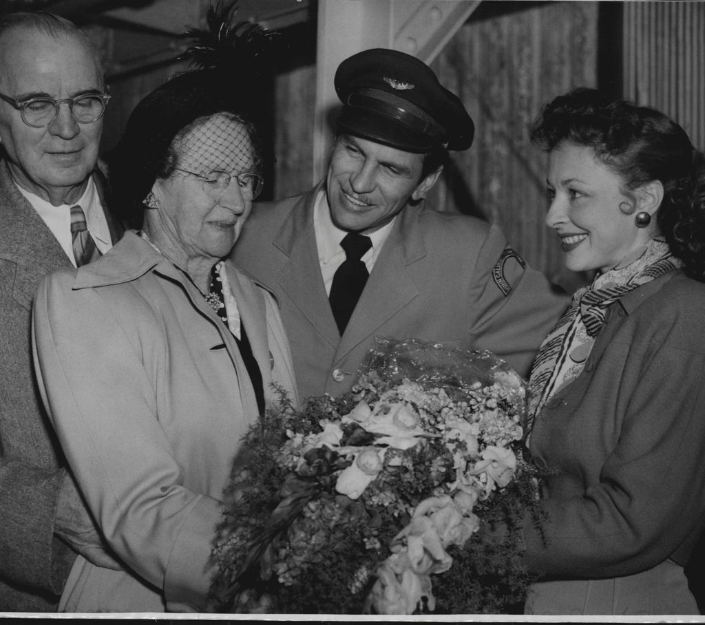 John Calvert wearing a hat and suit looking down with a smile at his mother.