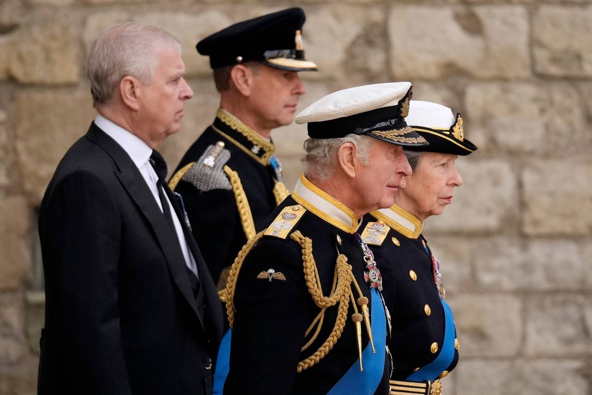 An image depicts three men in formal attire, two in military uniforms and one in a dark suit, standing together in a formal setting against a stone wall background.