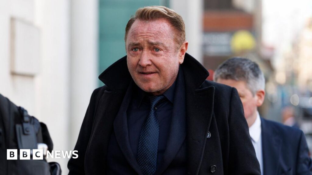 Lord of the Dance: Flately to obtain new sets and costumes Michael Flatley. He has short reddish hair, wearing a navy suit and black coat.