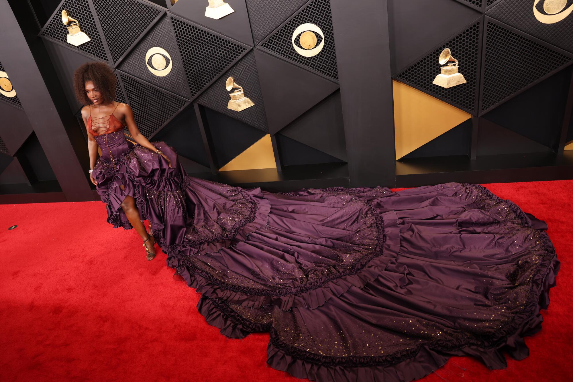 Doechii, wearing a deep purple gown with a long train, poses on the red carpet. 