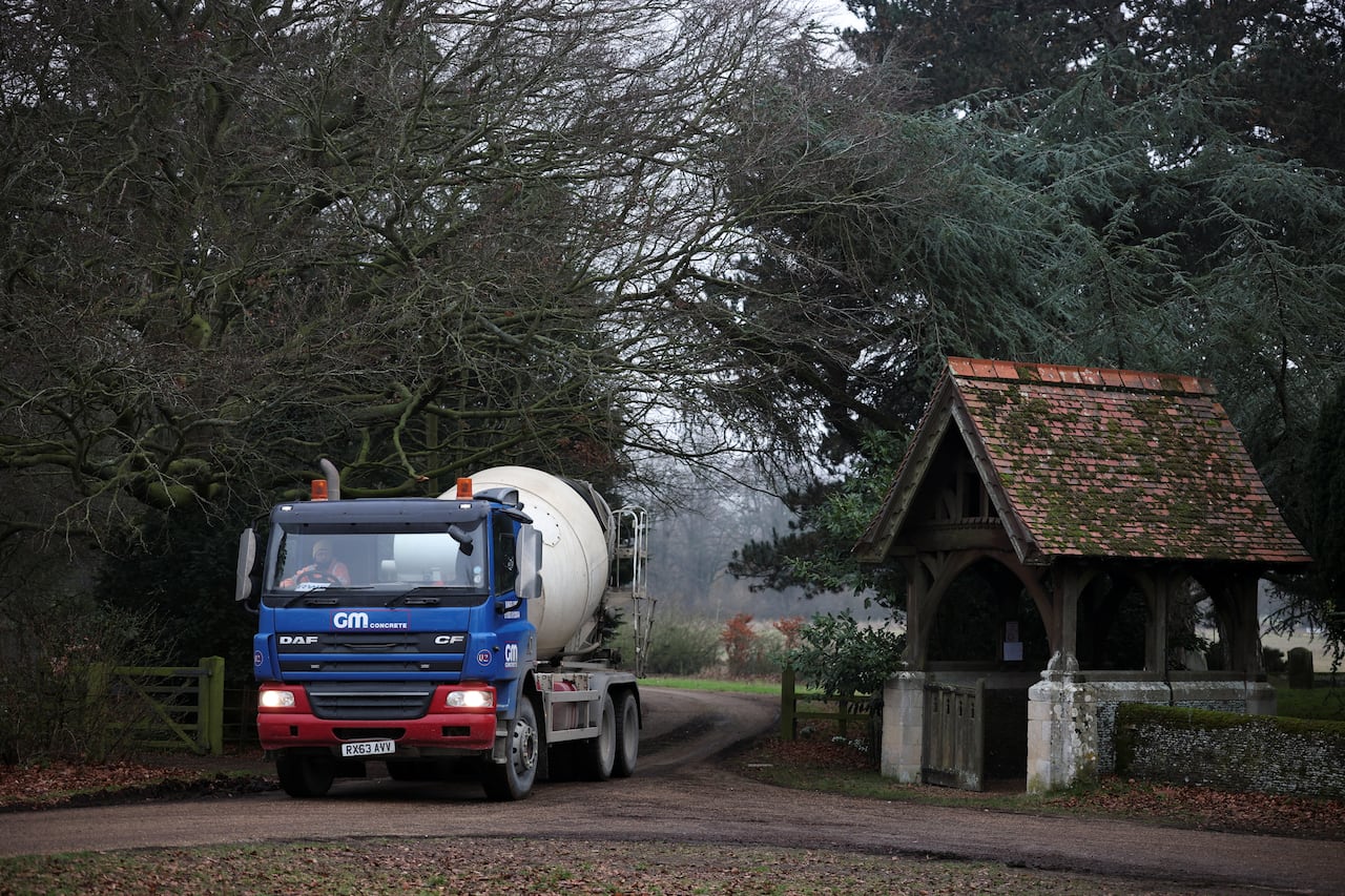 A truck drives down a road and though an entrance with a fence on either side.