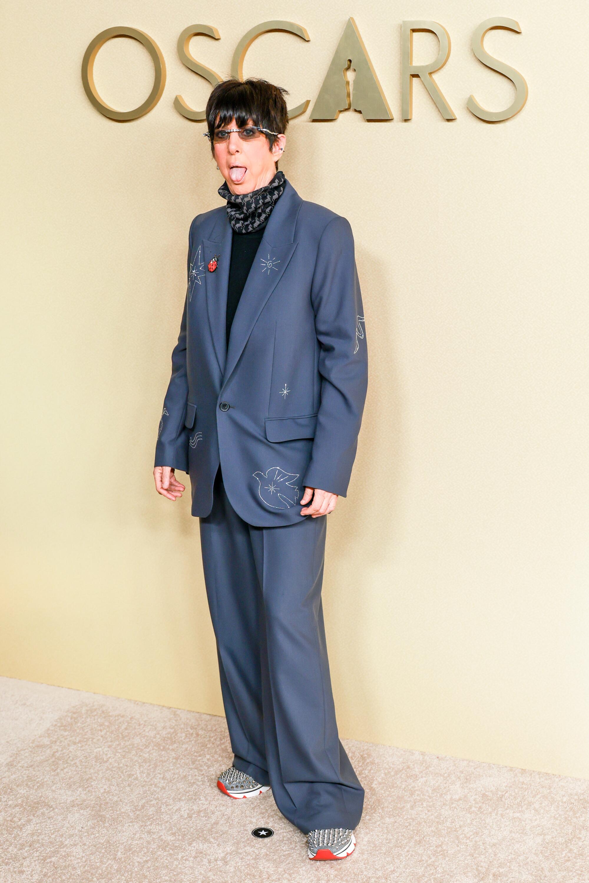 Diane Warren, wearing an oversized suit, poses on the beige carpet.
