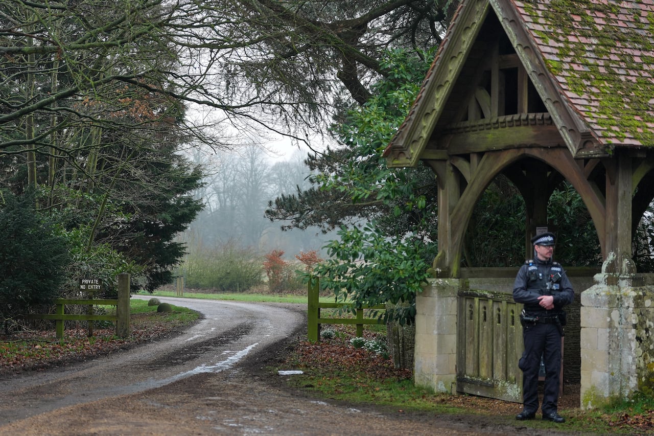 A police officer stands near an entrance to a rural property.