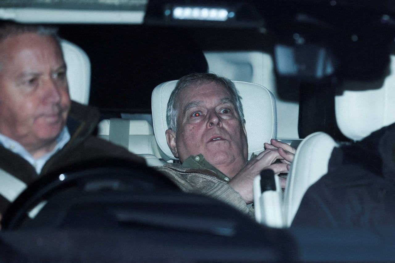 A person reclined in the back seat of a car is shown behind a person in the front seat.