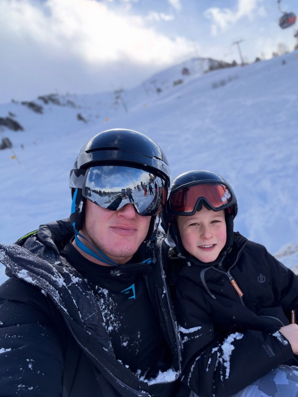 Matt Morsia and his son, Morsia, wearing ski suits and helmets