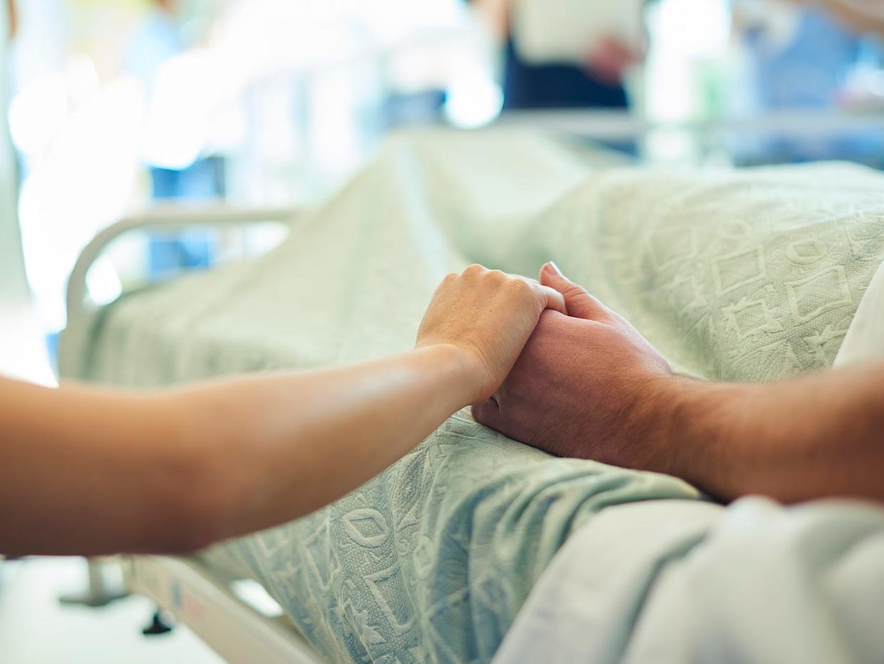 A visitor holding hands with a patient in a hospital bed.