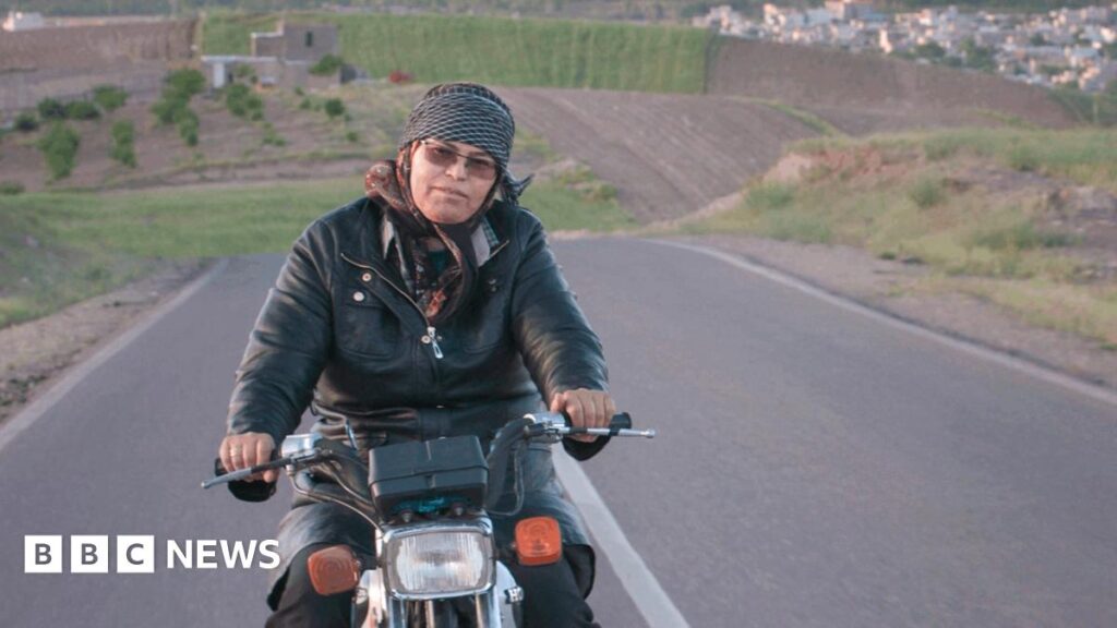 Cutting Through Rocks: Iran women defying norms in Oscar-tipped film A woman rides a motorcycle along an empty road, with rolling hills seen in the background.