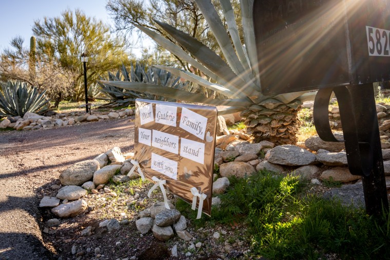 A beam of sunlight sweeps across a sign reading "DEAR GUTHRIE FAMILY, YOUR NEIGHBORS STAND WITH YOU."