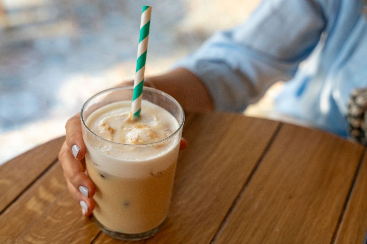 Woman holding glass of iced coffee with milk on blurred background.