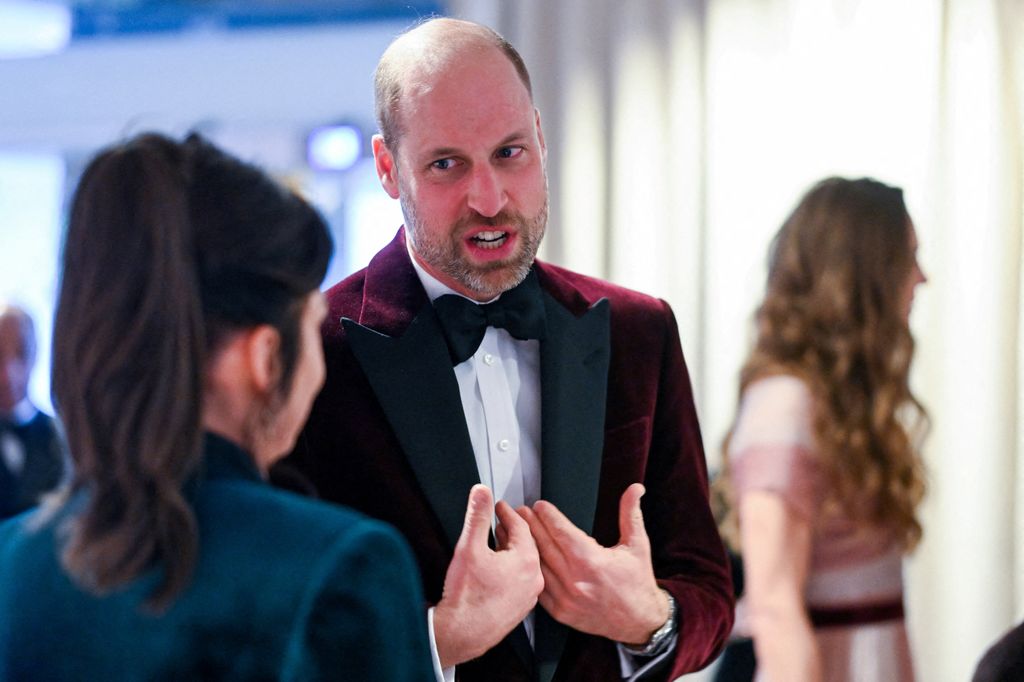Britain's Prince William, Prince of Wales, meets with Jane Millichip, CEO of the British Academy of Film and Television Arts. He is pictured speaking to her while wearing a maroon velvet suit.