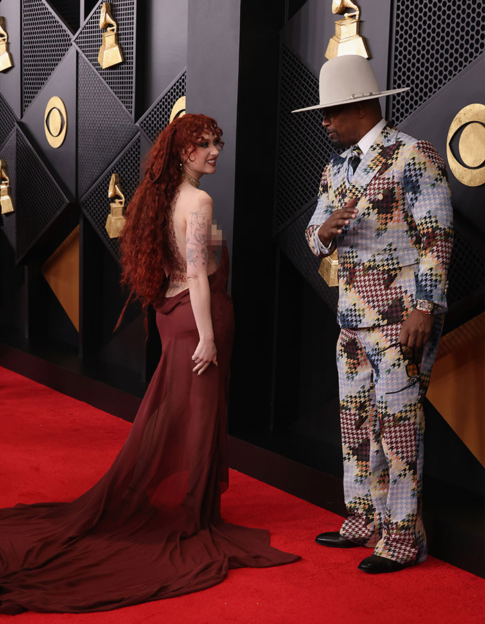 Jamie Foxx on the Grammy red carpet in a colorful suit interacting with Chappell Roan wearing a flowing maroon gown.