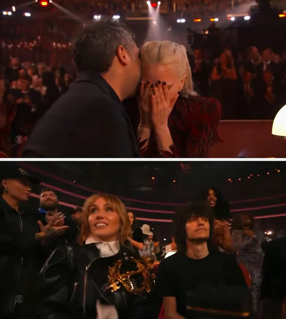 A person whispers to another with braided hair covering their face in surprise or joy, while seated in an event setting