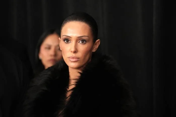 Person on red carpet wearing a faux fur stole, looking directly at the camera with a neutral expression