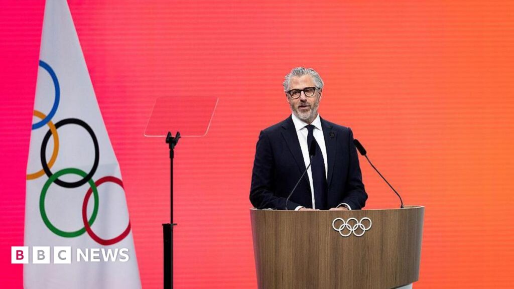 Casey Wasserman speaks to the media in Los Angeles in June 2025. He is wearing a black sweatshirt and glasses.