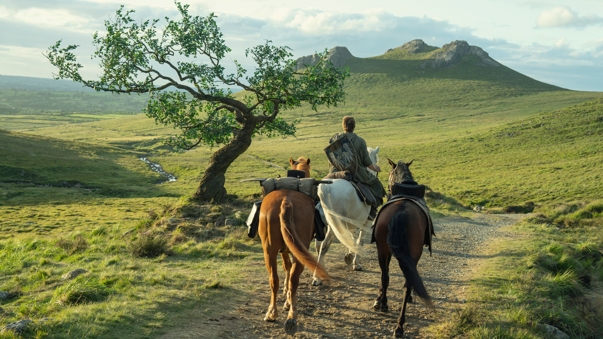 Ser Dunk (Peter Claffey) riding a horse away from the camera along a dirt road with two other horses in tow in a promotional still for "A Knight of the Seven Kingdoms"
