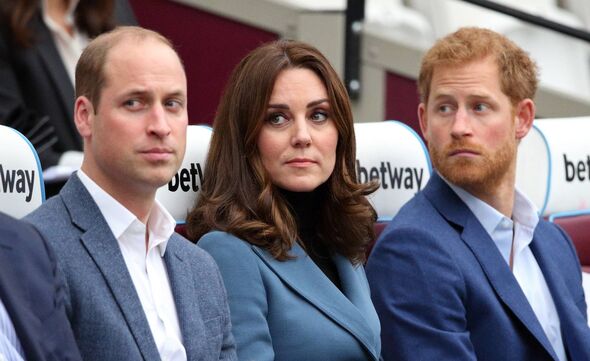 Three individuals dressed in formal attire are seated together in a stadium. The individuals are positioned next to one another,