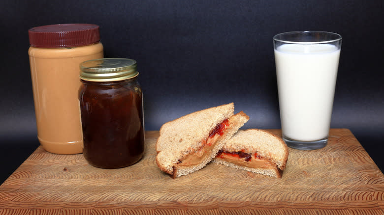 Jars of peanut butter and jelly next to a PB&J and a glass of milk