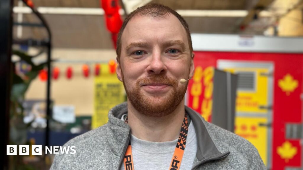 KPop Demon Hunters: Belfast animator inspiring young people James is smiling at the camera. He is wearing a grey t-shirt and hoodie and has an orange lanyard around his neck.