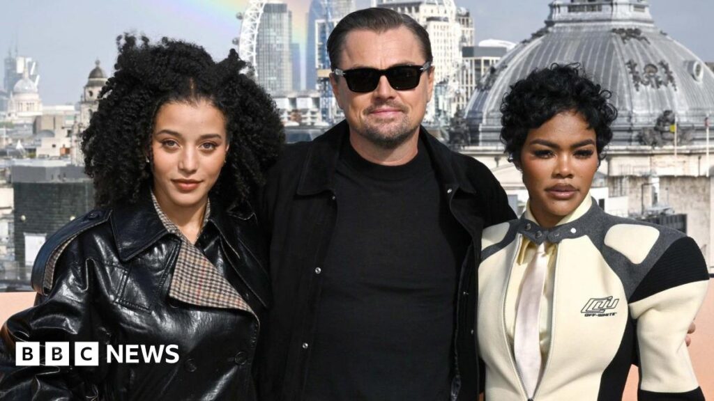 Chase Infiniti, Leonardo DiCaprio and Teyana Taylor at a promo event in London last year. Infiniti is wearing a black PVC jacket, DiCaprio is wearing a black T-shirt and jacket with sunglasses, while Taylor has on a racing-style cream and black zipped jacket.