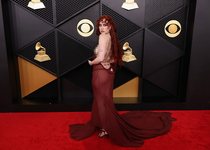 Chappell Roan in a flowing maroon gown posing on the Grammy red carpet with Grammy and CBS logos in the background.