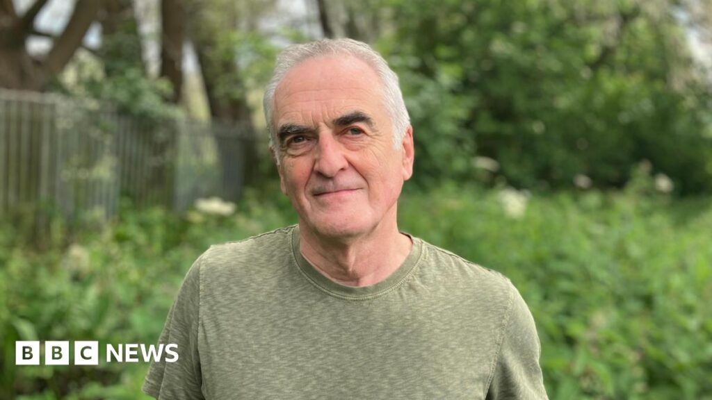 Ash Smith looking at the camera - he's got white hair, black eyebrows and is wearing a green T-shirt. He's white.