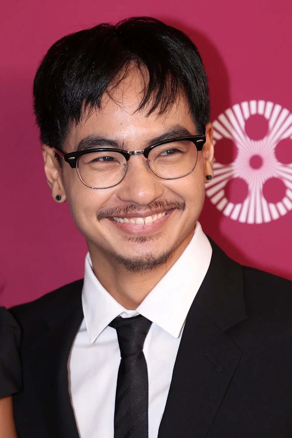 Person wearing glasses and a suit with a tie, smiling at a formal event