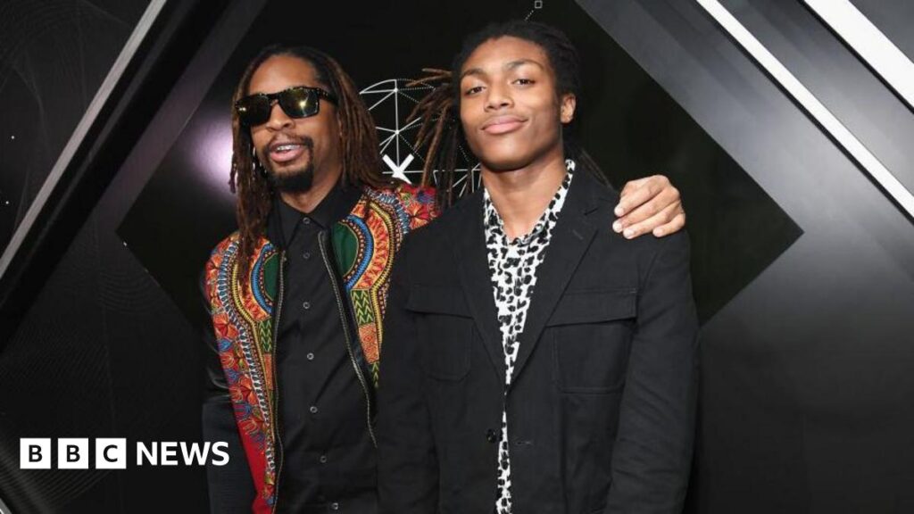 Rapper Lil Jon poses for a photo with his sone Nathan Smith. Jon wears a colourful jacket and black shirt while Smith is dressed in black and white