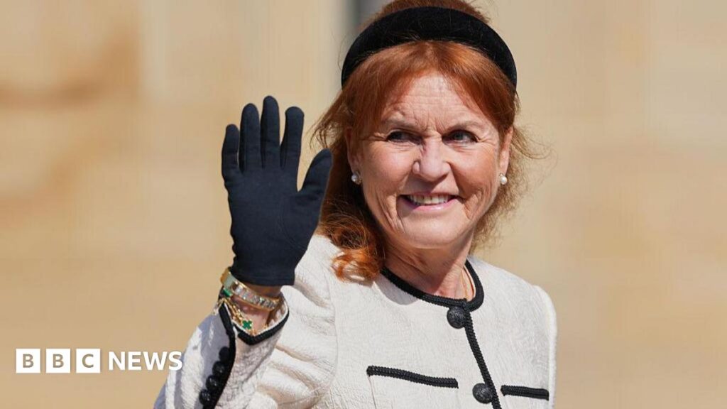 Six of Sarah Ferguson’s companies are being dissolved Sarah Ferguson waves her black-gloved hand while wearing a black headband, a cream jacket with a black trim, and large pearl earrings.