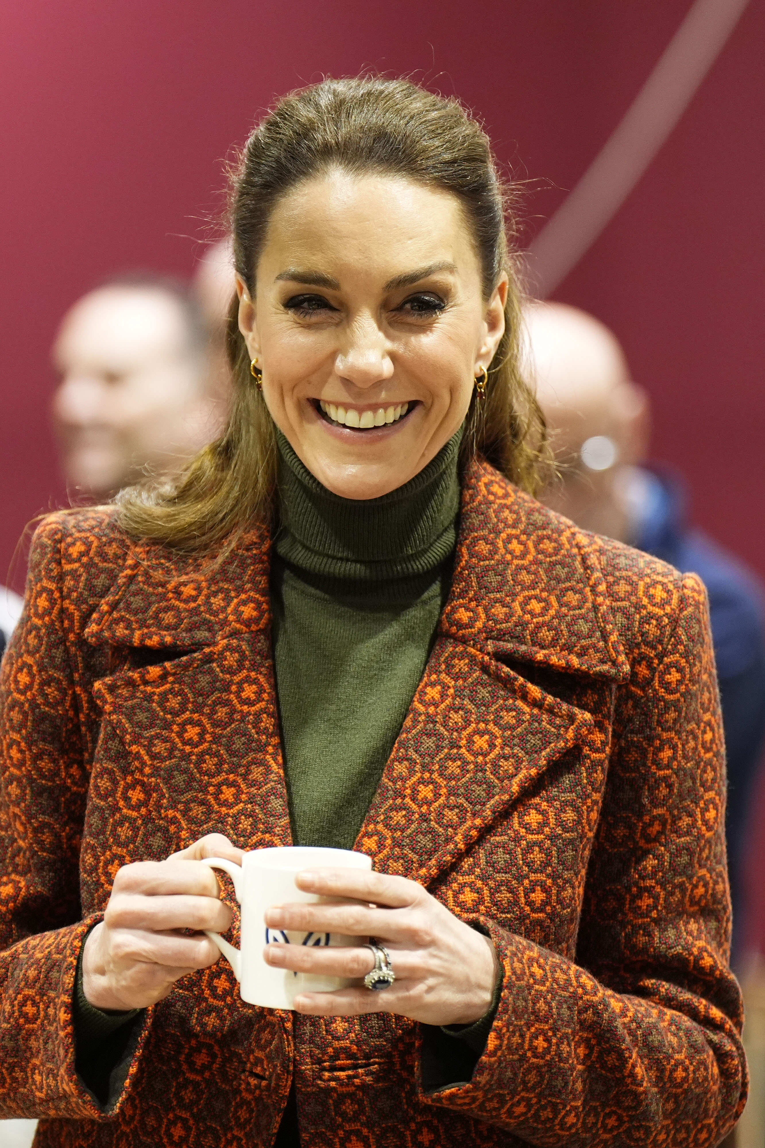 Princess Kate wearing an orange coat holding a coffee mug