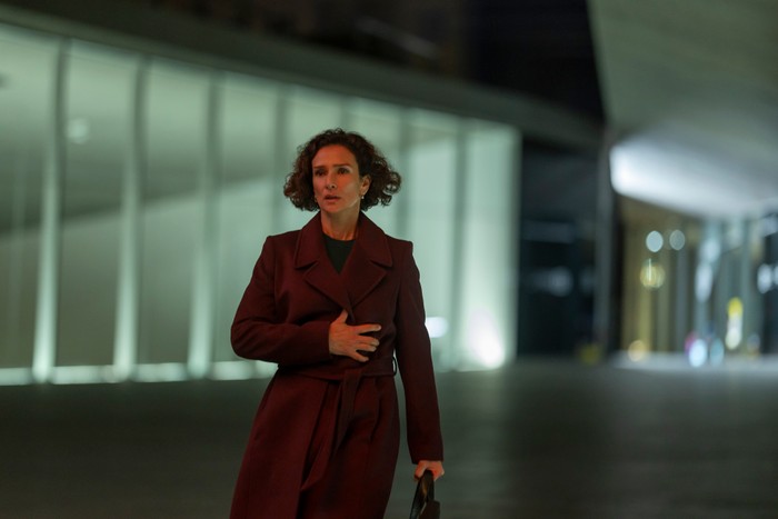 The Night Manager S2 Indira Varma in The Night Manager season 2, wearing a red coat, stood outside at night and looking shocked.
