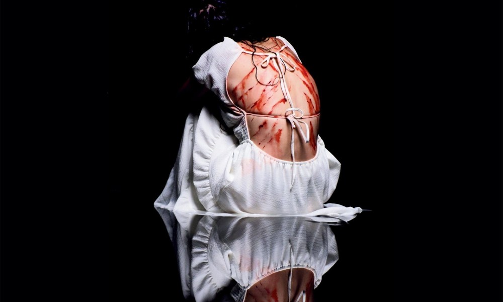 Foreigner trailer and poster reveal, featuring down crouched in white backless dress exposing bloody claw marks