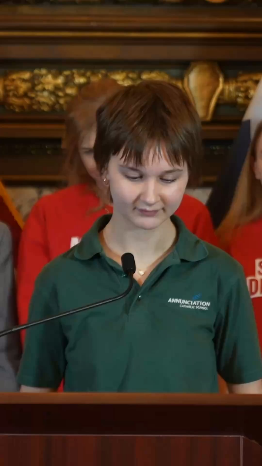 Lydia Kaiser, an 8th-grade survivor of gun violence, stands up on the stage with Tim Walz and states:  “116 bullets through the stained-glass windows. 2 students shot and killed. 2 survived gunshots injuries to the head. I am one of them… elected officials have a duty to protect us from guns.”